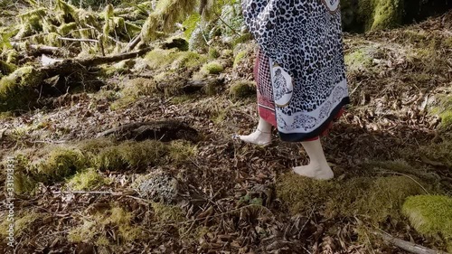 Woman shaman walking barefoot from right to left on moss covered rainforest ground while thanking her ancestors for her abundance photo