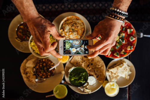 Sticker man's hands taking photo with a smartphone of indian food on the table, top view