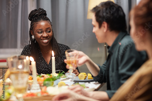 Young African woman smiling and talking to her friends while they sitting at the table and eating dinner
