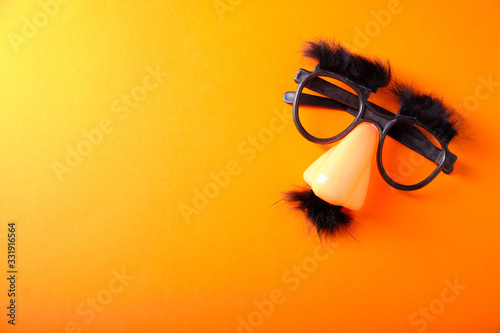 Overhead glasses, nose and mustache for April 1, April Fool's Day, on orange background