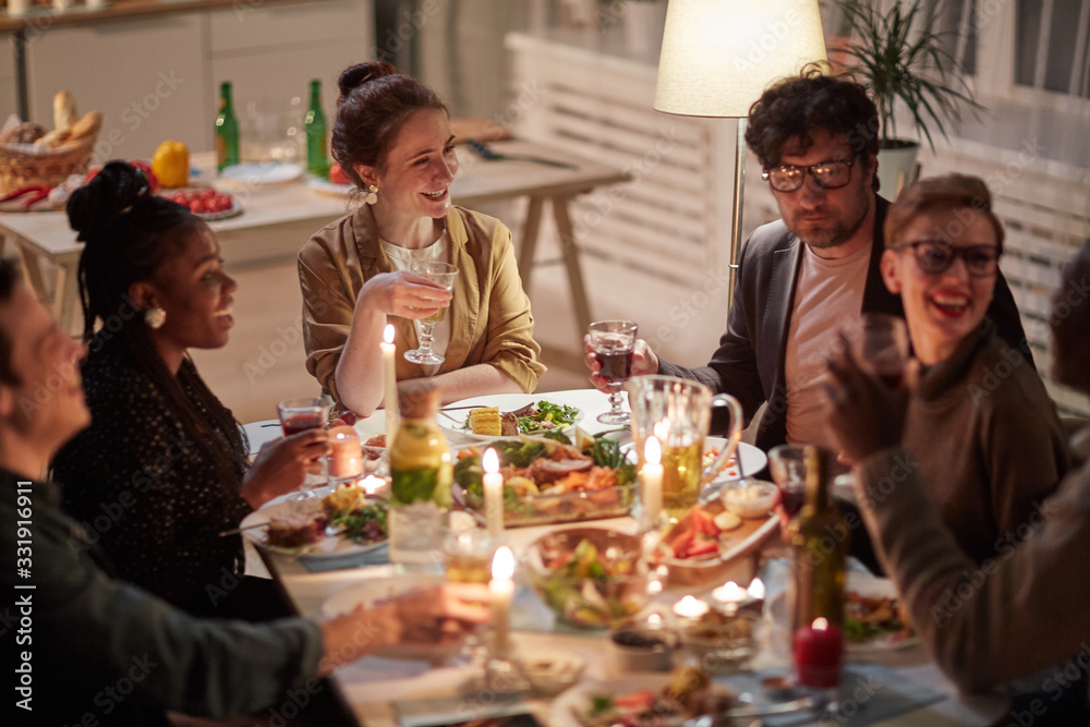 Group of happy friends laughing and talking during holiday dinner at the table at home