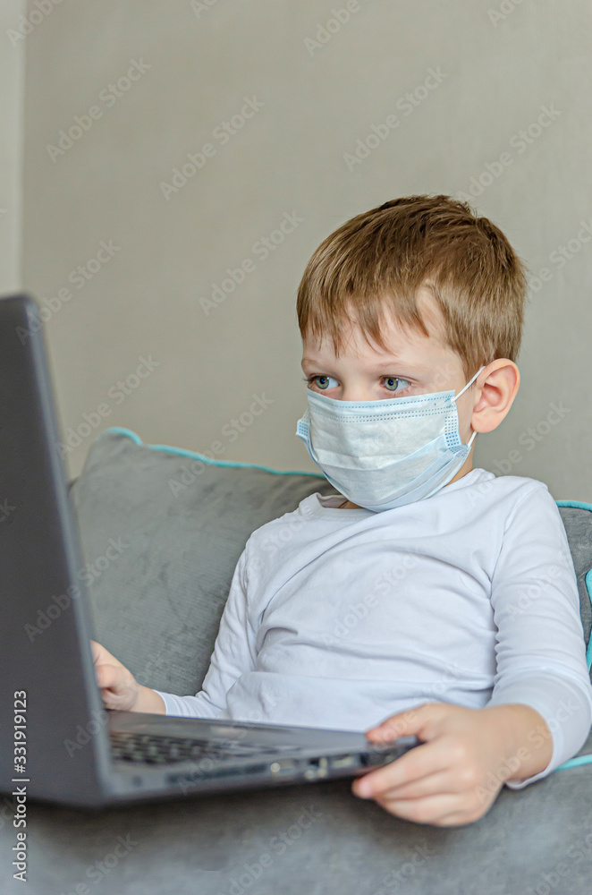 Quarantined children. Self isolation. A child in a medical mask watches cartoons on a laptop while sitting on a sofa. Quarantined children. Self isolation. A child in a medical mask watches cartoons on a laptop while sitting on a sofa.