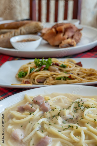 The dish of spaghetti , white sauce carbonara and frird pork leg with sausages served in the white dishes on the red tartan table in the redtaurant.  photo