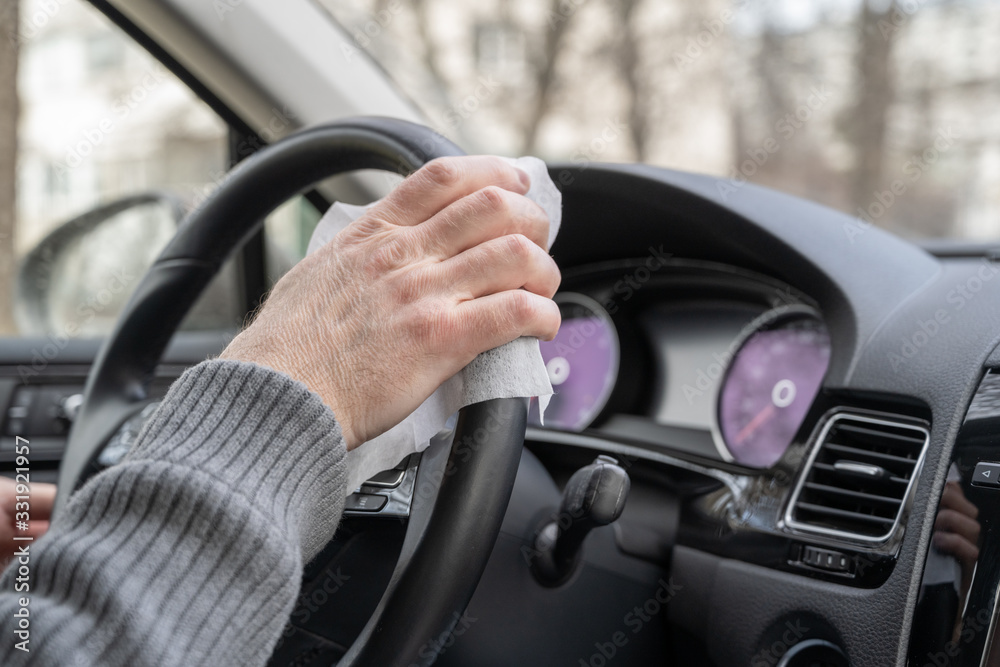 Man cleaning steering wheel of a car using antivirus antibacterial wet wipe (napkin) for protect himself from bacteria and virus.