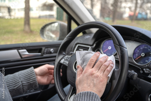 Man cleaning steering wheel of a car using antivirus antibacterial wet wipe (napkin) for protect himself from bacteria and virus.