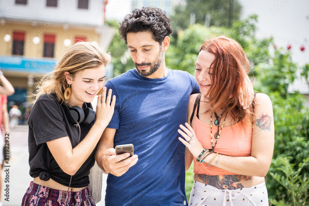 three friends looking at their cell phones while smiling on the street