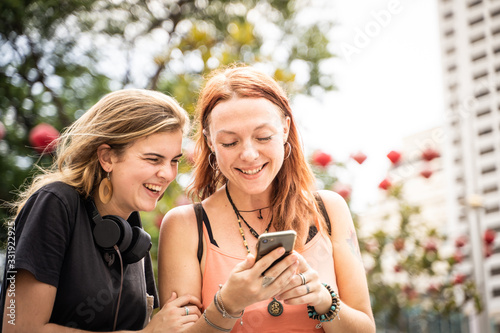 Two young women looking at the mobile phone while laughing in the street