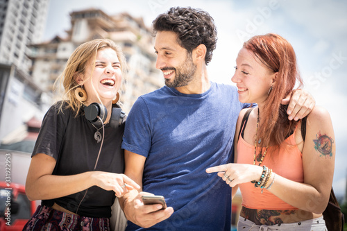 three friends laughing and looking at the mobile on the street