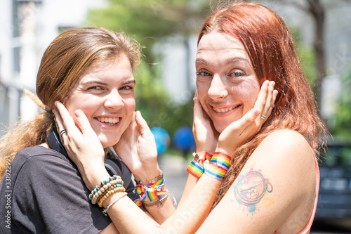Couple of women caressing each other s faces while smiling and wearing a lgtb flag bracelet
