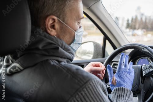 Man in the medical mask puts on rubber gloves for protect himself from bacteria and virus while driving a car. Coronavirus. Pandemic