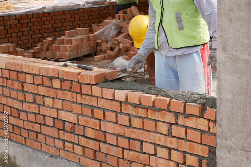 Brickwork by construction workers at the construction site. Workers laying the clay brick and stacked it together using mortar to form the wall. 