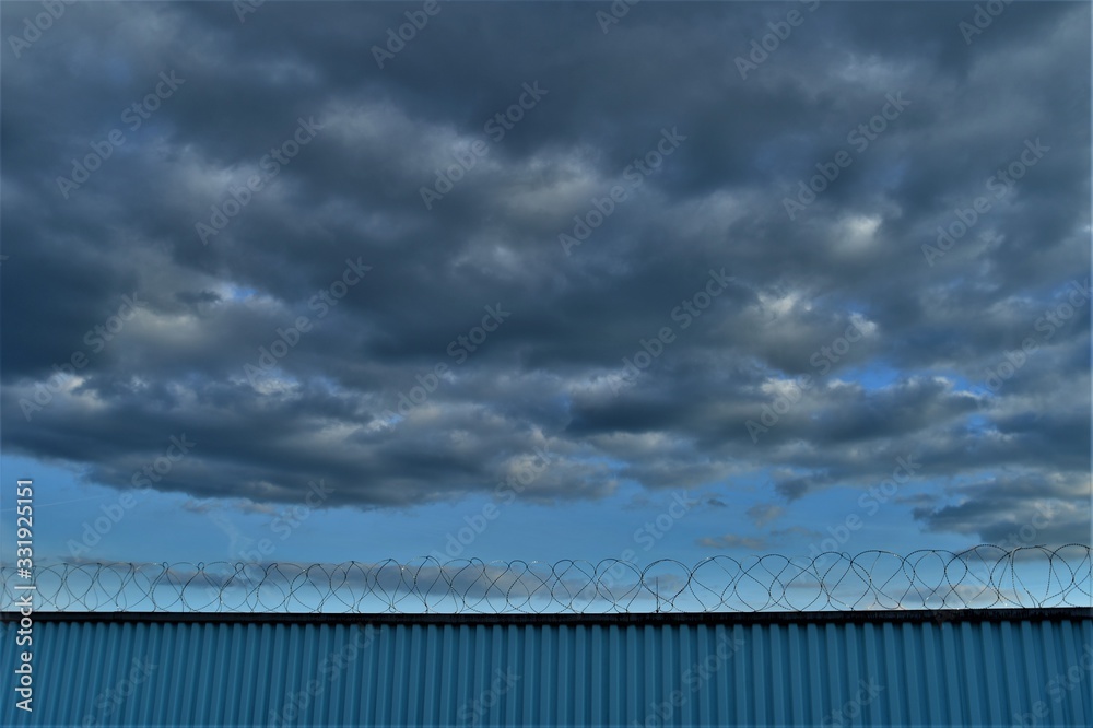 blue fence with barbed wire under a blue sky with clouds