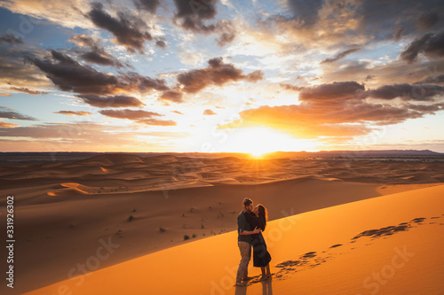 Couple in love kissing in Sahara desert dunes, Morocco. Happiness, freedom and escape concept. Amazing warm sunset with beautiful colorful clouds.