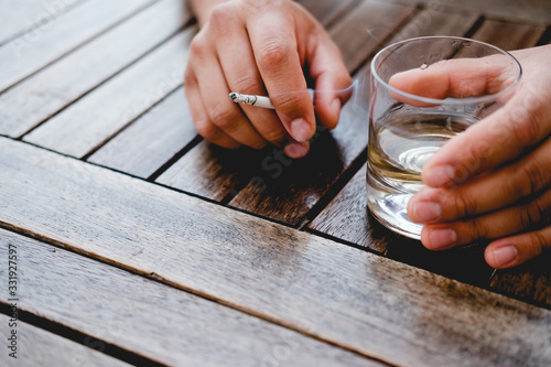 a man is holding a glass with a drink and a cigarette. pernicious habits. hazardous to health.