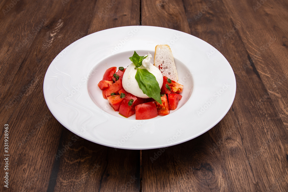 Fresh Burrata cheese with tomatoes on a plate on a wooden table. Fresh Burrata cheese with tomatoes on a plate on a wooden table.