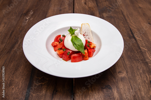 Fresh Burrata cheese with tomatoes on a plate on a wooden table.