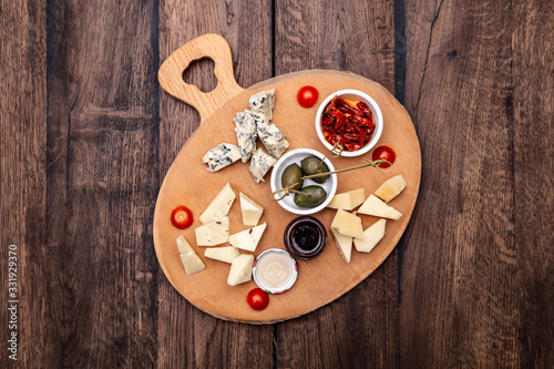 Different types of delicious cheese, olives, jam and sun-dried tomatoes on a wooden board. Top view.