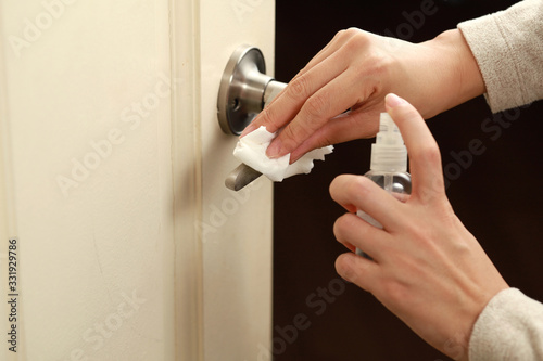 Close up view of female hand using antibacterial wet wipe for disinfecting home room door link.