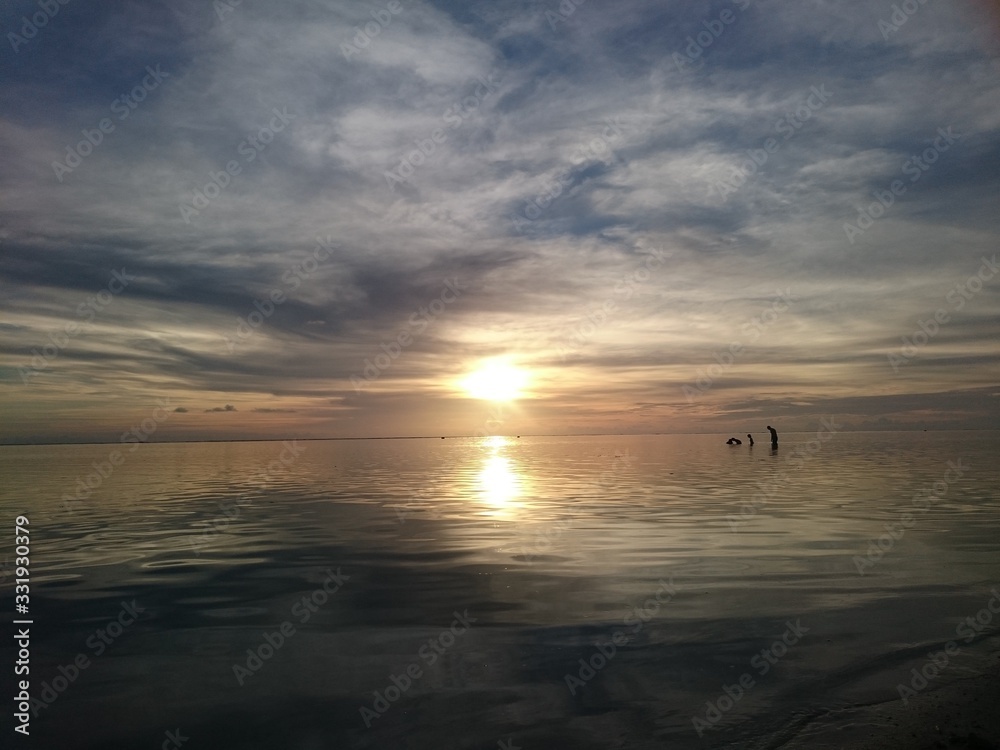 Sunset with people standing in the water 