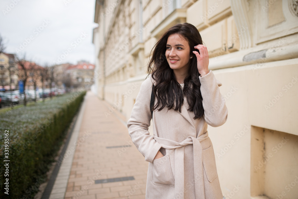 Fototapeta premium girl in a coat walks down the street and looks from the side