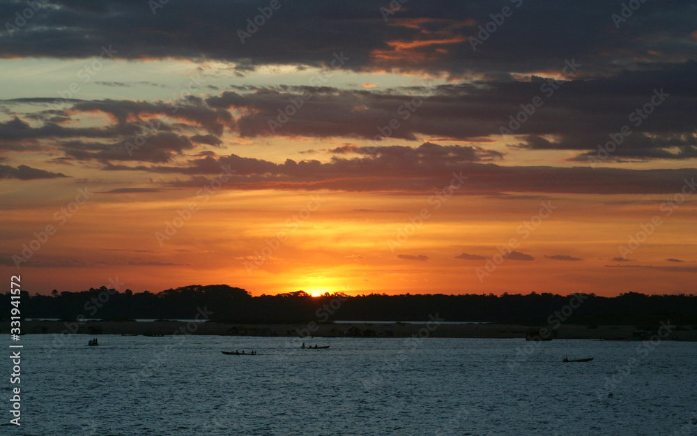 Pôr-do-sol em praia de margem de rio, com degradê laranja no céu e silhueta de barcos pequenos