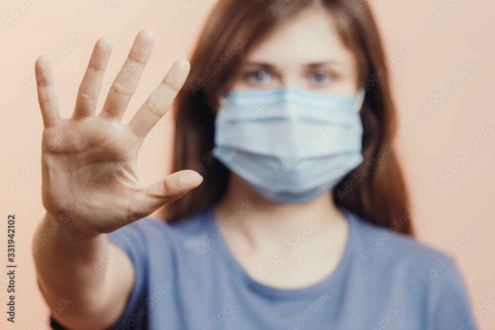 young woman in medical protective mask shows a stop gesture with hand on studio background, girl held out palm with fear, concept of quarantine measures young woman in medical protective mask shows a stop gesture with hand on studio background, girl held out palm with fear, concept of quarantine measures