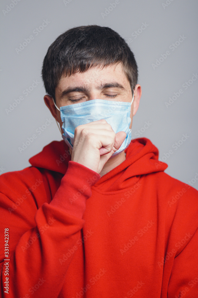 Man in medical mask coughing on gray studio background, concept of prevention viral deseases, person in red sweatshirt with breathing problems Man in medical mask coughing on gray studio background, concept of prevention viral deseases, person in red sweatshirt with breathing problems