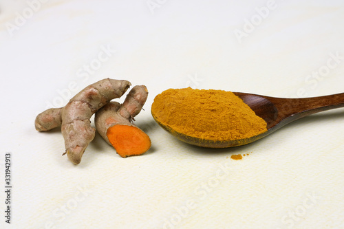 Turmeric powder in a wooden spoon and fresh turmeric roots isolated on a white background is an ingredient in turmeric foods and ingredients in skin care products. Turmeric helps the skin to be strong