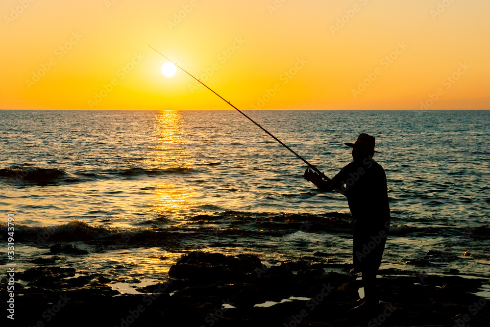 Fisherman at sunset throws tackle into the sea. Silhouette of a fisherman fishing at sunset