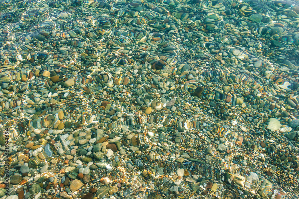 Colored pebbles under clear sea water. Sea bottom under the blue water of the sea, background