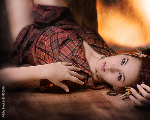Joven campesina acostada sobre el piso de madera con decoración de pelillos de tender de madera y en pose tranquila y sexy con camisa a cuadros carmelita photo