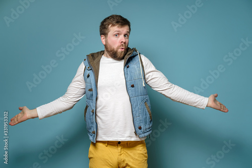 Quadro em tela Caucasian man is surprised and bewildered, he throws up hands in perplexity and looks confusedly, on a blue background