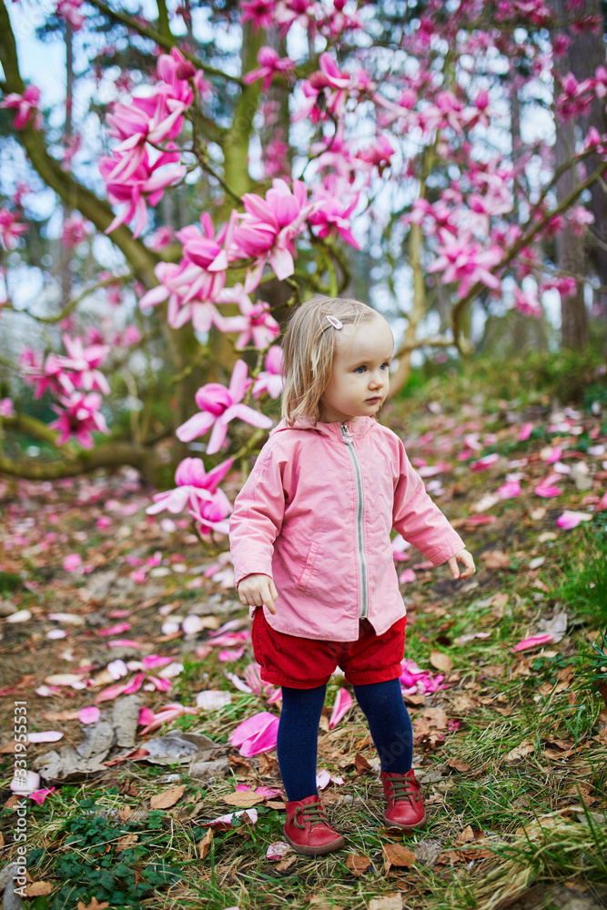 Adorable toddler girl near giant magnolia in full bloom Adorable toddler girl near giant magnolia in full bloom
