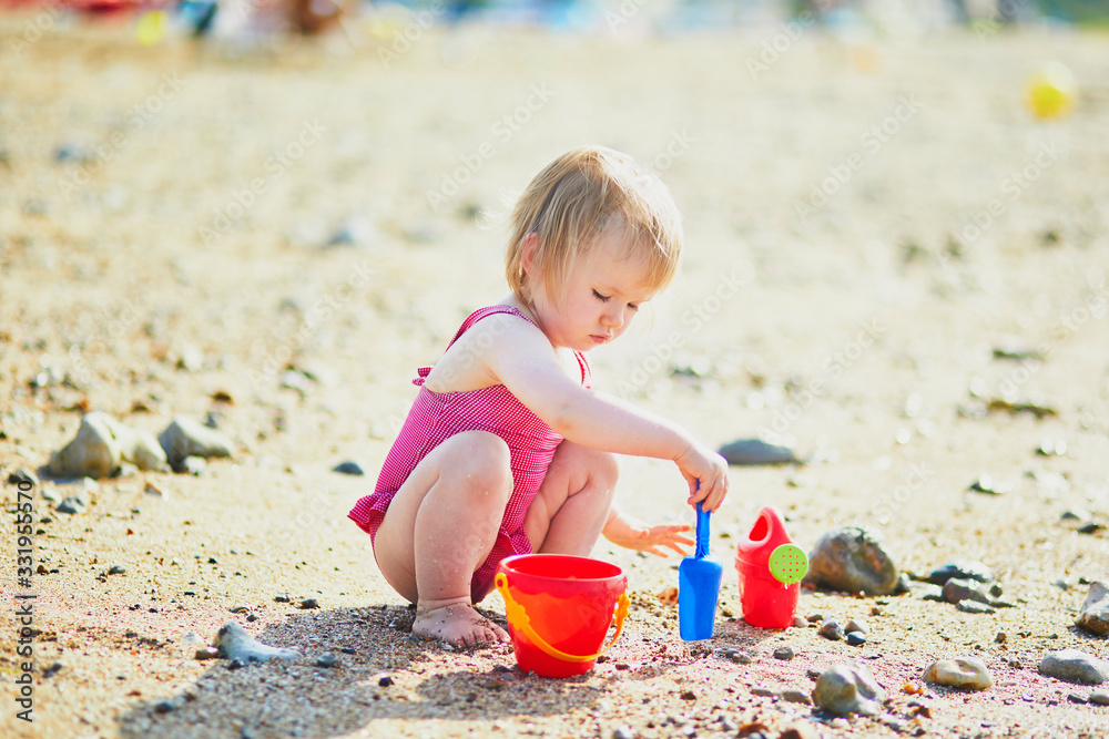 Adorable toddler girl playing with sand on the beach. Child spending vacation on the Atlantic coast in Normandy, France. Outdoor activities for kids Adorable toddler girl playing with sand on the beach. Child spending vacation on the Atlantic coast in Normandy, France. Outdoor activities for kids