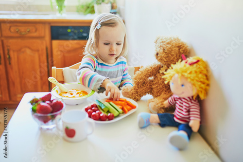 Adorable toddler girl eating fresh fruits and vegetables for lunch