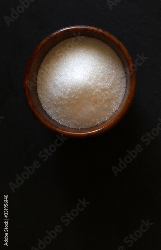 Zucchero bianco in una ciotola di legno, isolata su fondo scuro. Vista dall'alto.