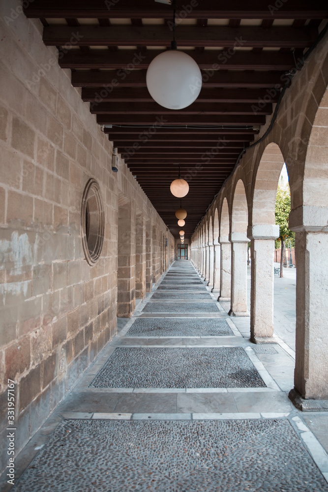 Obraz premium A Beautiful Perspective of an Aisle with Brick Walls on the left, Arches and Garden on the right and Stripes of Wooden Ceiling on top