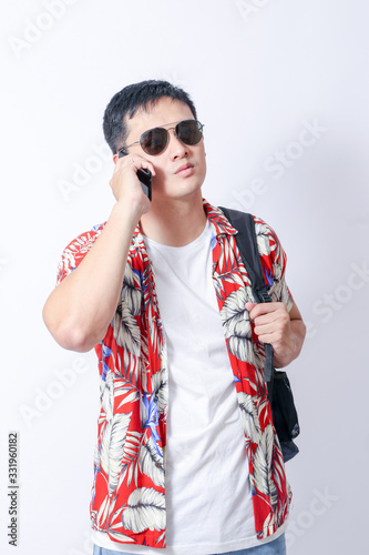 A Portrait of young tourist asian man wearing floral shirt and showing gesture sign. or laptop, Smartphone, camera  and wallet stand in isolated background