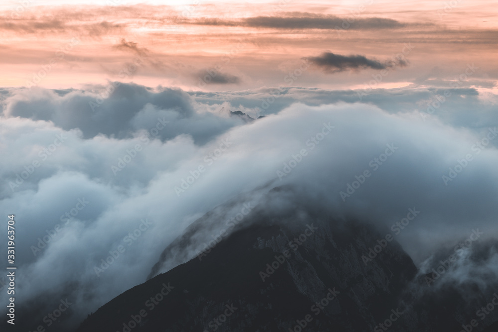 Background photo of low clouds in a mountain valley, vibrant blue and orange sky. Sunrise or sunset view of mountains and peaks peaking through clouds. Winter alpine like landscape of Slovenian Alps