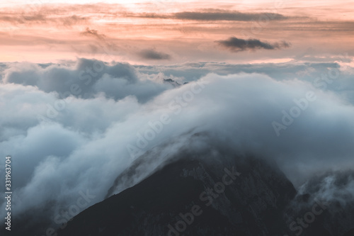 Background photo of low clouds in a mountain valley, vibrant blue and orange sky. Sunrise or sunset view of mountains and peaks peaking through clouds. Winter alpine like landscape of Slovenian Alps