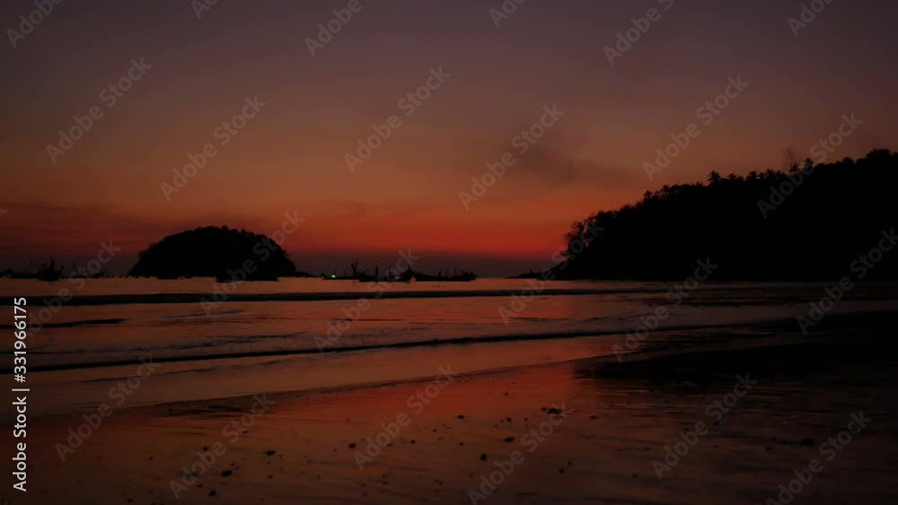 soft sea wave breaking sand beach, silhouette tree mountain on right, island in the ocean, long tail fishing boat parking in water, at twilight colorful orange evening time after sunset soft sea wave breaking sand beach, silhouette tree mountain on right, island in the ocean, long tail fishing boat parking in water, at twilight colorful orange evening time after sunset