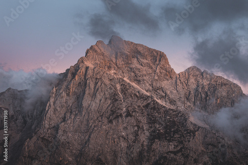 Background photo of low clouds in a mountain valley, vibrant blue and orange pink sky. Sunrise or sunset view of mountains and peaks peaking through clouds. Winter alpine landscape of Slovenian Alps