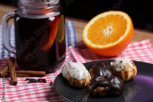 Glass of mulled wine, eclairs on a black plate, orange , cinnamon and cloves isolated on a black background.