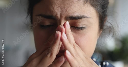 Close up exhausted frustrated young indian woman massaging nose bridge temples. Stressed unhealthy millennial mixed race girl feeling tired suffering from migraine, panic attack, high blood pressure.