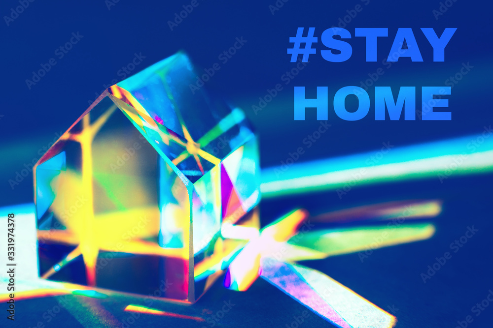 Closeup of colorful glass prism house on trendy blue background with rainbow light refraction and shadows with text STAY HOME. Concept of prevention the coronavirus from spreading. Closeup of colorful glass prism house on trendy blue background with rainbow light refraction and shadows with text STAY HOME. Concept of prevention the coronavirus from spreading.