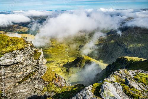 View down the Coire Aonaich from the top of Ben Lui on a cloudy day. Scenic Scottish summer aerial landscape with low clouds and green valley below.