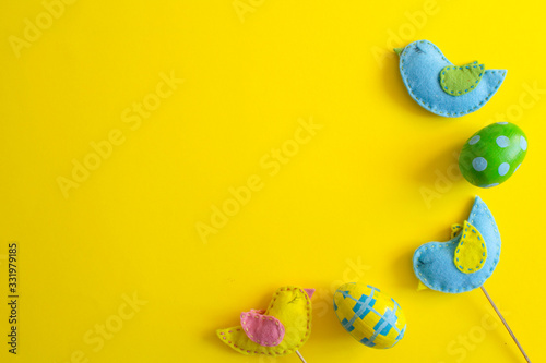 Spring home decor. Easter concept. Handmade yellow and blue felt birds and easter eggs on sticks on yellow background.flat lay,overhead,top view,copy space, place for text