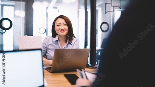 Happy ethnic businesswoman using laptop and looking at camera in boardroom