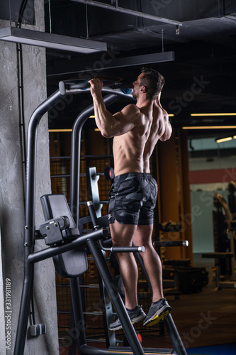 Muscular sexy young man doing exercise for the back on horizontal bar