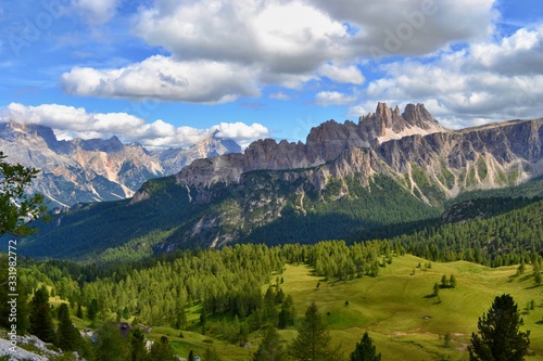 Dolomites mountains, Italy. Sunny day, blue sky, white clouds, green grass. 